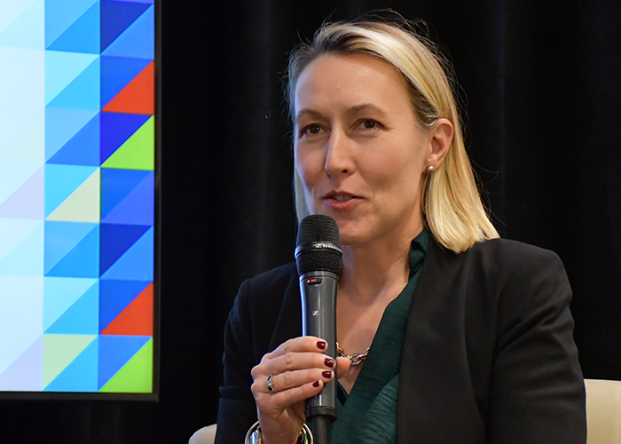 Maggie Arvedlund Marcus sits on stage at the MWBE Conference and speaks into a microphone.